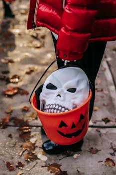 A child carries a pumpkin bucket with a skull mask during a Halloween street celebration.