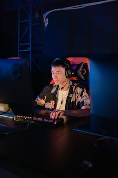 A young man intensely playing an online game at a gaming setup in a dimly lit room.