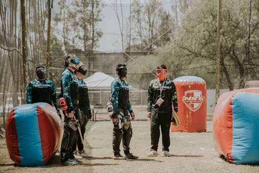 Group of men in paintball gear planning next moves in an outdoor field.