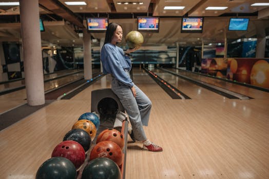 Woman standing in a bowling alley holding a bowling ball, classic leisure activity.